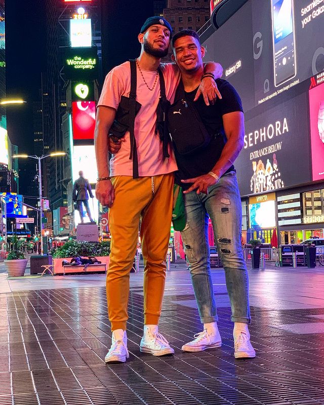 Sarunas J. Jackson in a pink t-shirt and orange pants hugging his brother in a black t-shirt and blue jeans.